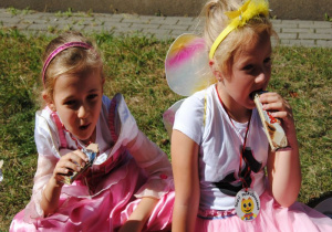 dziewczynki przebrane za księżniczkę i pszczółkę jedzą batony siedząc na kocu w ogrodzie